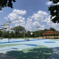 Basketball hoops on a light blue court with blue sky and white clouds