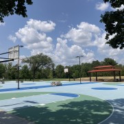 Basketball hoops on a light blue court with blue sky and white clouds
