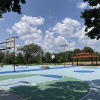 Basketball hoops on a light blue court with blue sky and white clouds